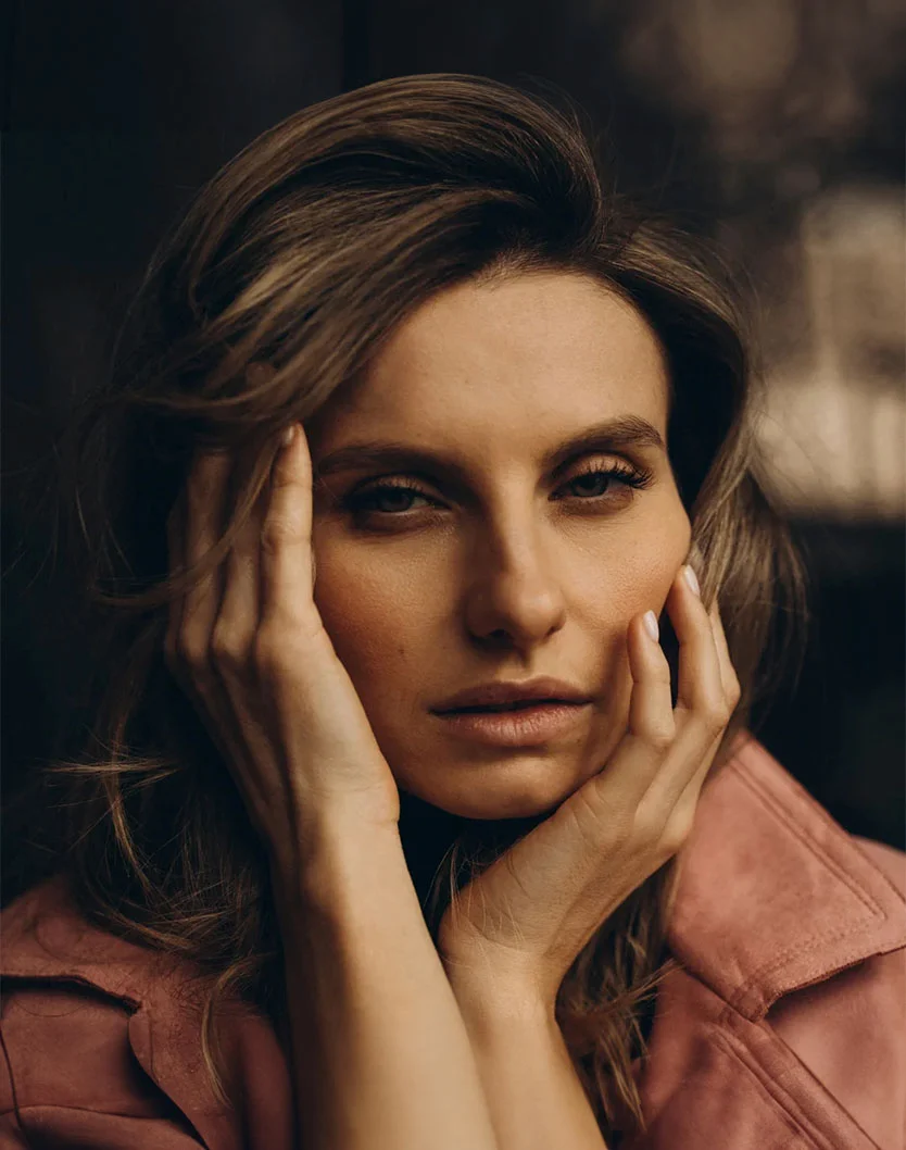 A close-up portrait of a woman with wavy hair, resting her face on her hands, conveying a thoughtful expression. - Facial Fat Transfer in New York, NY